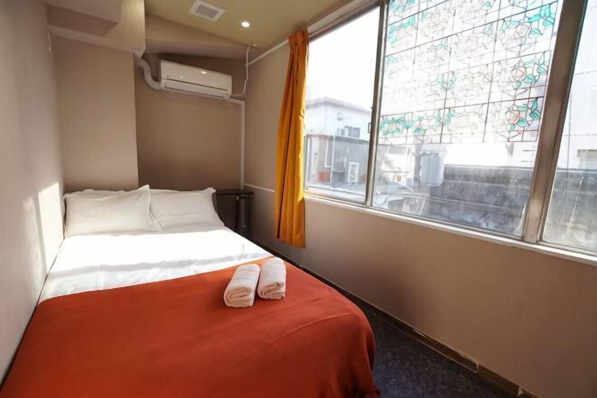 A hotel room with a bed, a window with curtains, and an air conditioning unit.