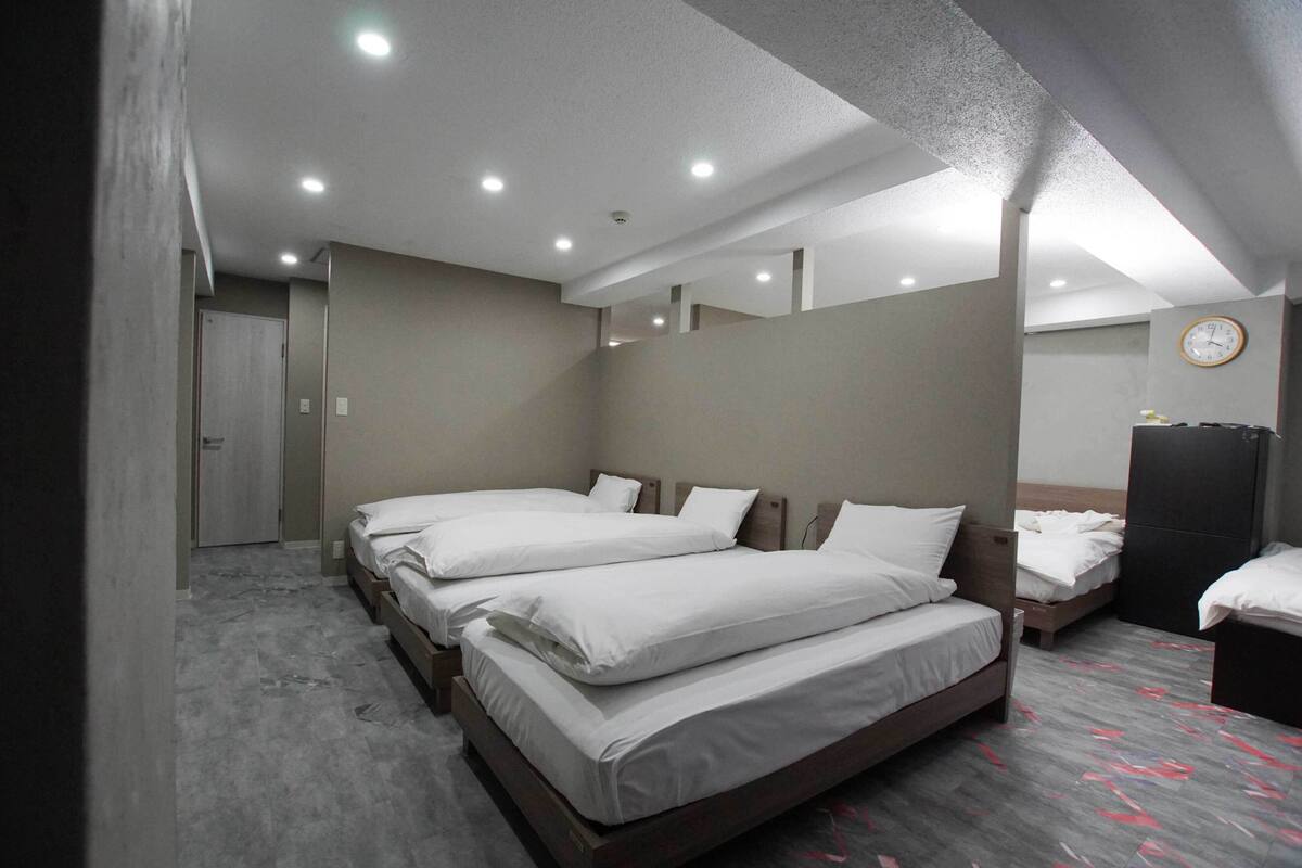 A hotel room with three single beds, a wooden wardrobe, a clock on the wall, and a door leading to another room.