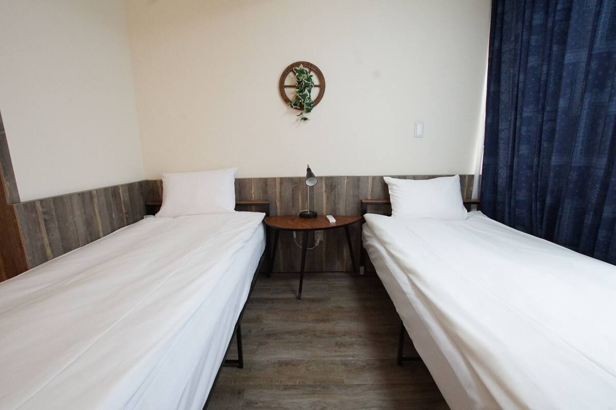 A hotel room with two single beds, a small round table, and a wall-mounted plant.