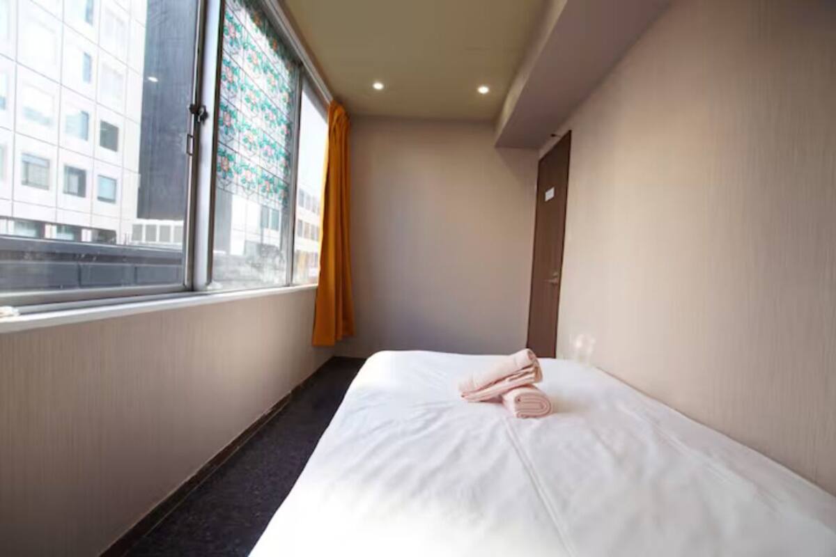 A hotel room with a large window, a bed with neatly folded towels, and a door to the right.