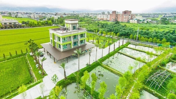 A modern building with a flat roof, surrounded by lush green fields and a water body. - Beautiful Village (Wujie)