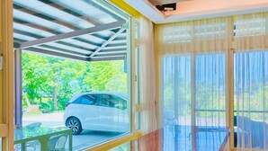 A modern interior with a long wooden table, large windows, and a view of a parked car outside.