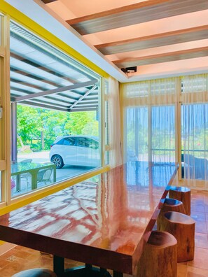 A modern interior with a long wooden table, large windows, and a view of a parked car outside. - Beautiful Village (Wujie)