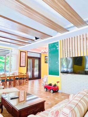 Una stanza con soffitto in legno, un divano, un tavolo da pranzo con sedie, una piccola macchinina rossa e una lavagna appesa al muro.