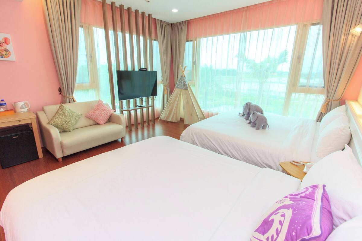A hotel room with two beds, a TV, a sofa, and a tent.