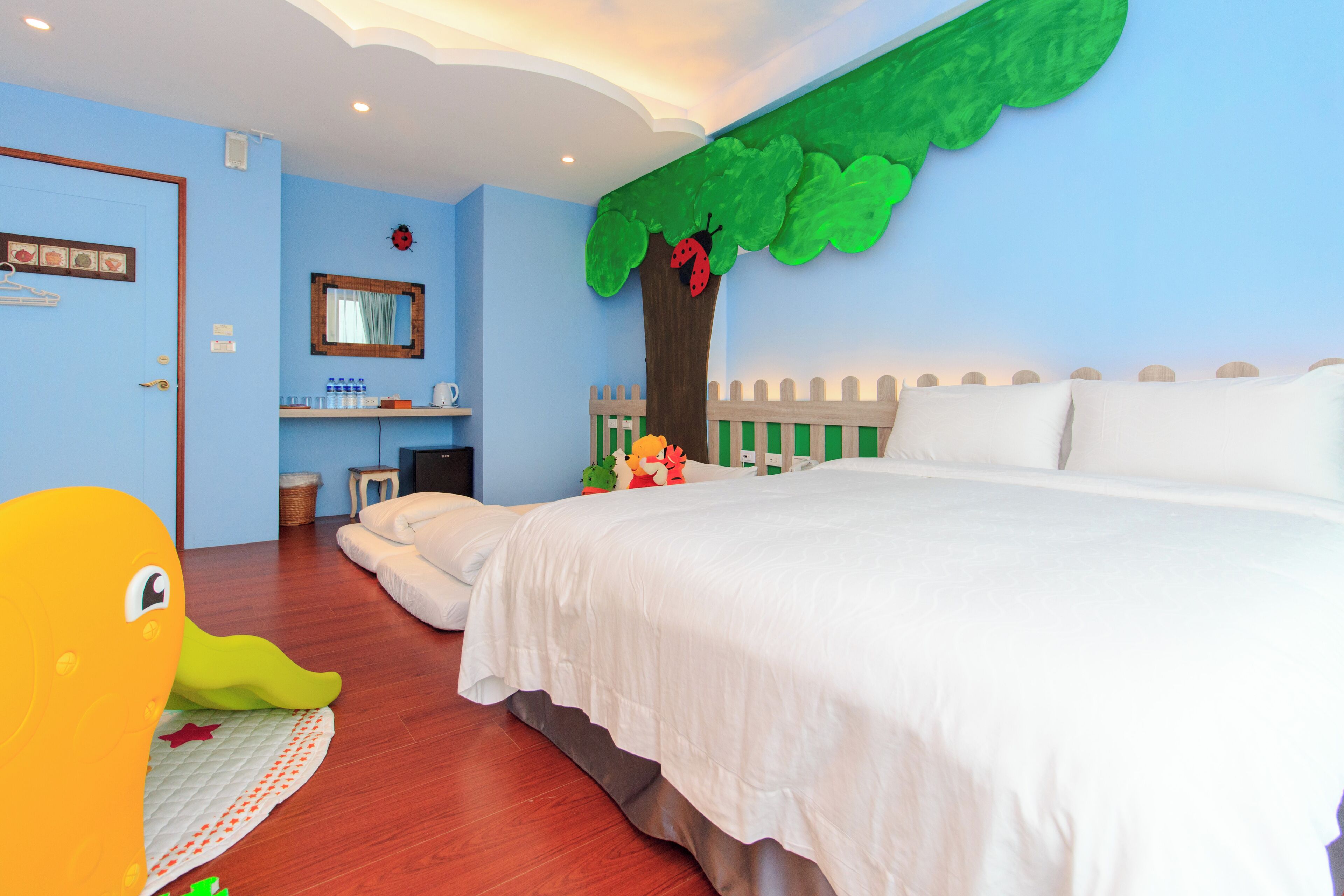 Une chambre à coucher avec un grand lit, une commode, un miroir et un mur décoré d’un motif représentant un arbre et une clôture.