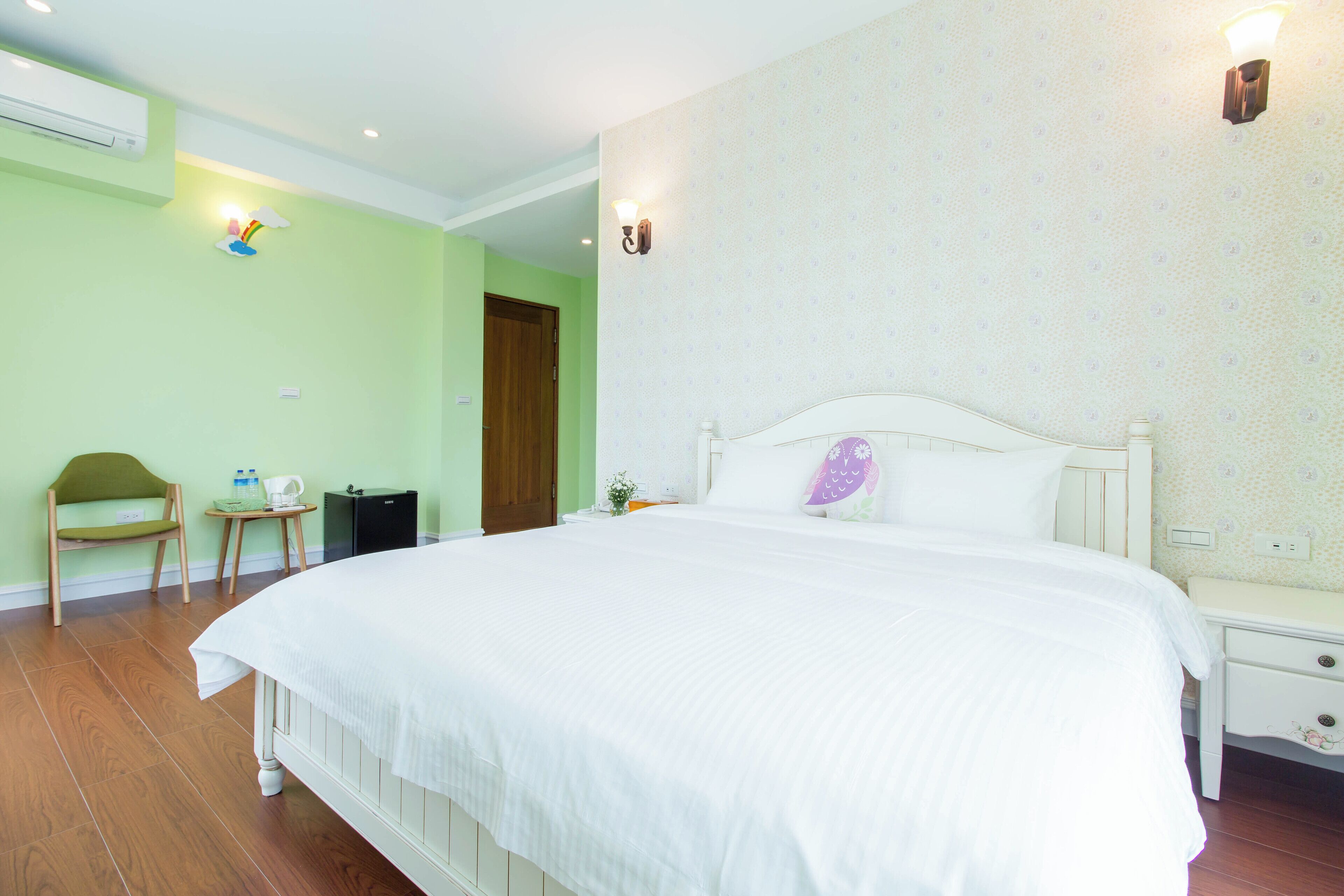 A bedroom with a large bed, a bedside table, a chair, and a small table with a lamp.