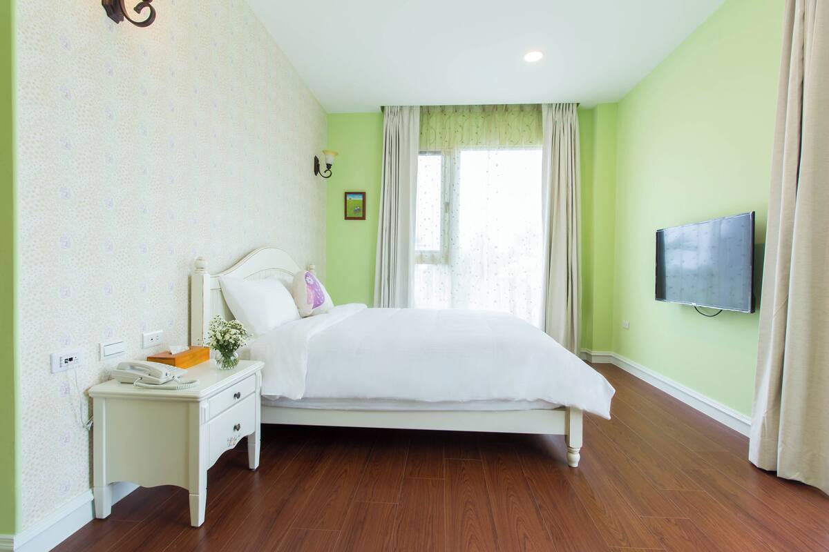 A bedroom with a bed, bedside table, lamp, and a television on the wall.