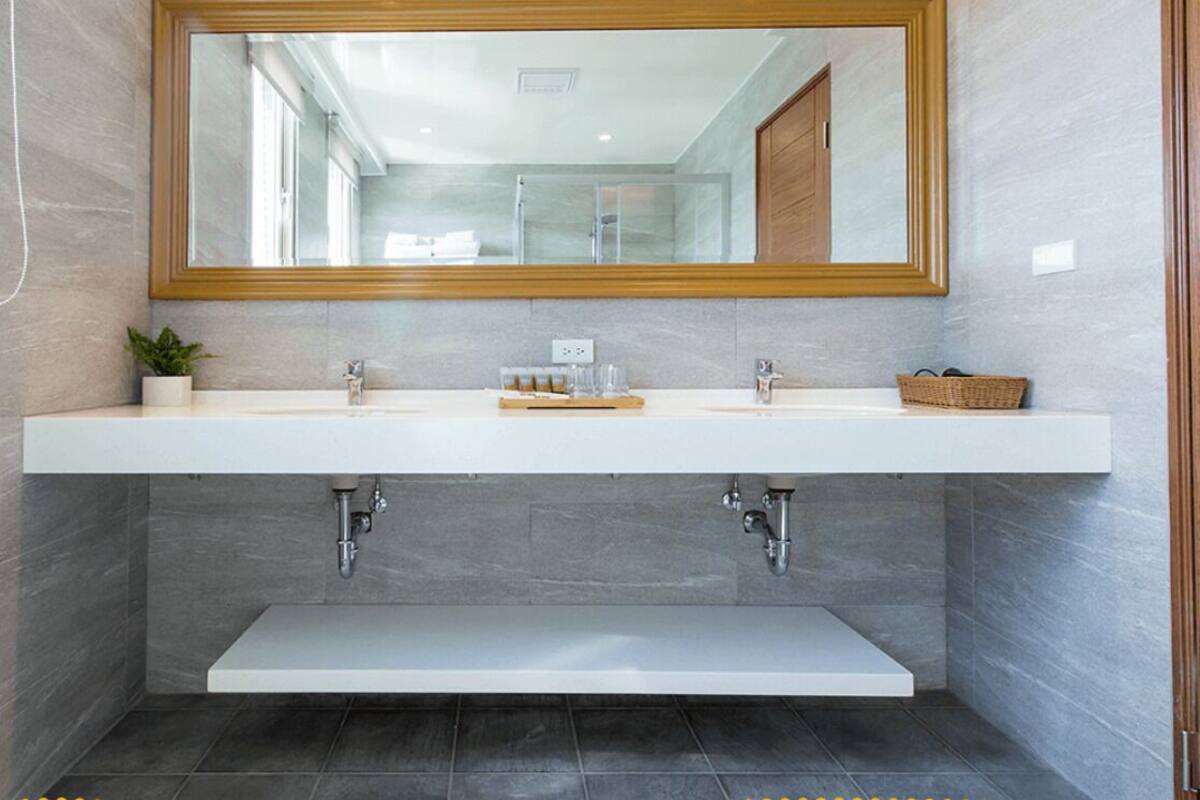 A modern bathroom with a large mirror, two sinks, a shelf below, and a shower area.