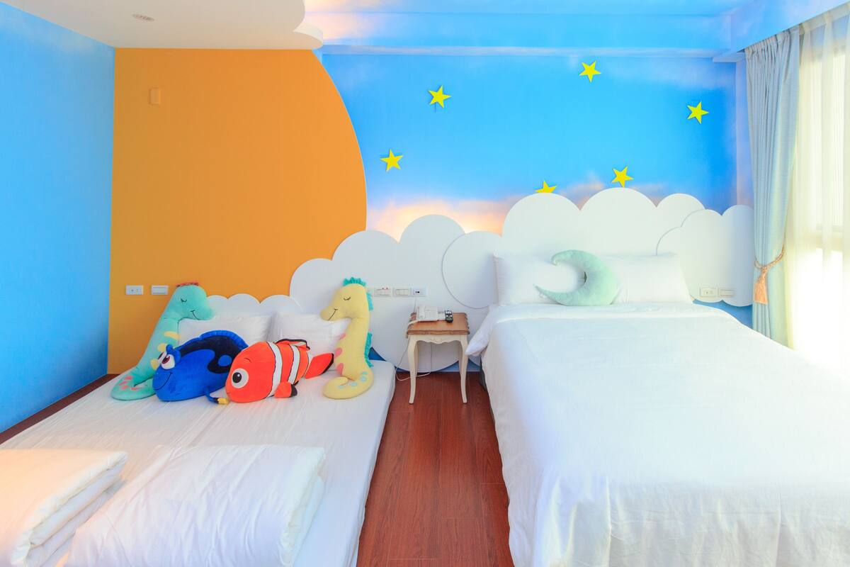 A hotel room with two beds, a nightstand, and a wall with a cloud and star decoration.