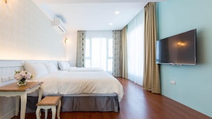 A hotel room with a large bed, a small table with a bench, a TV mounted on the wall, and a window with curtains. - Beautiful Village (Wujie)