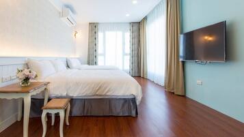 A hotel room with a large bed, a small table with a bench, a TV mounted on the wall, and a window with curtains.