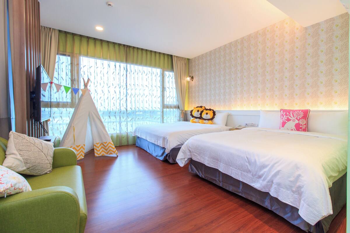 A hotel room with two beds, a green sofa, a tent, and patterned wallpaper.