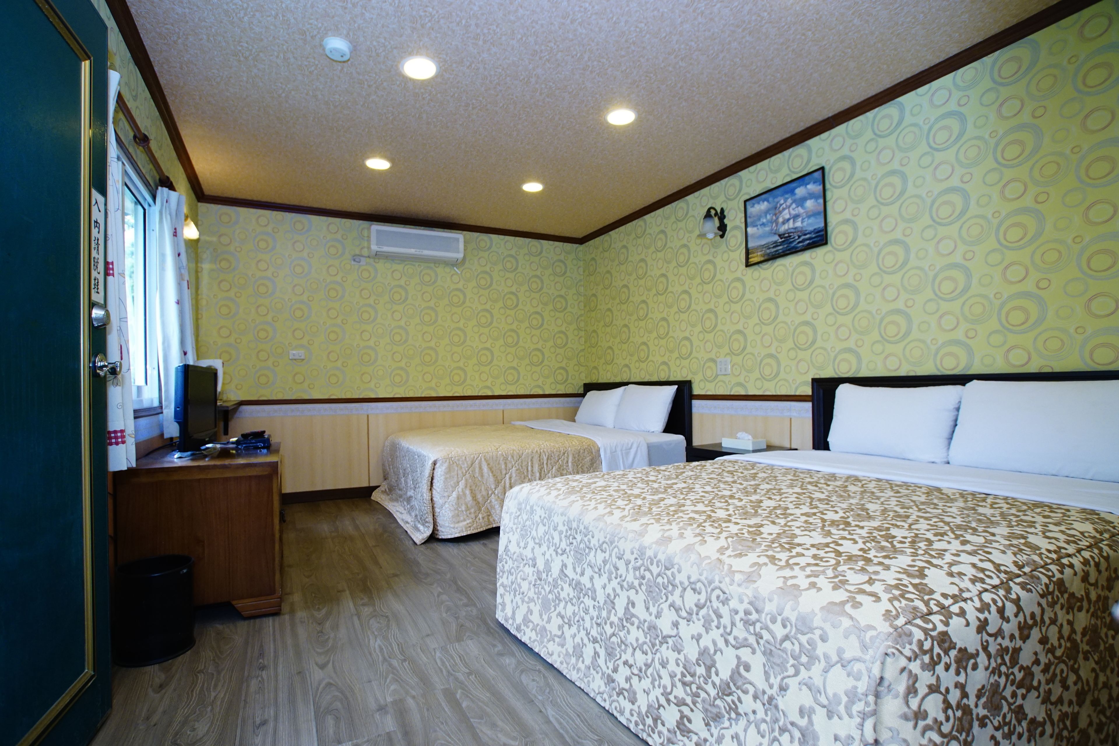 A hotel room with two single beds, a desk with a computer, and a small trash bin.