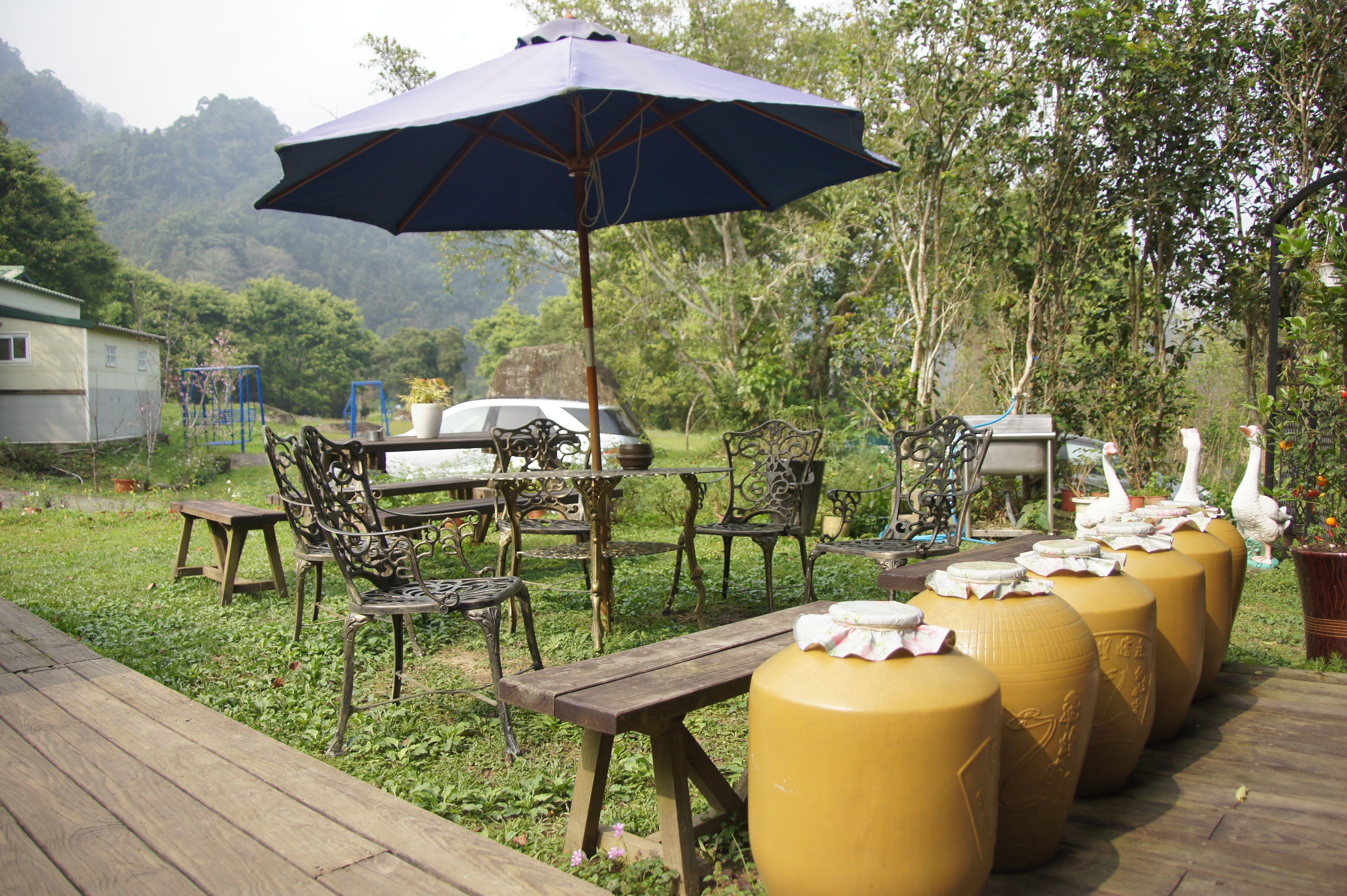 An outdoor seating area with wooden tables and chairs, a large umbrella, and decorative vases.