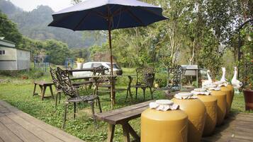 An outdoor seating area with wooden tables and chairs, a large umbrella, and decorative vases.