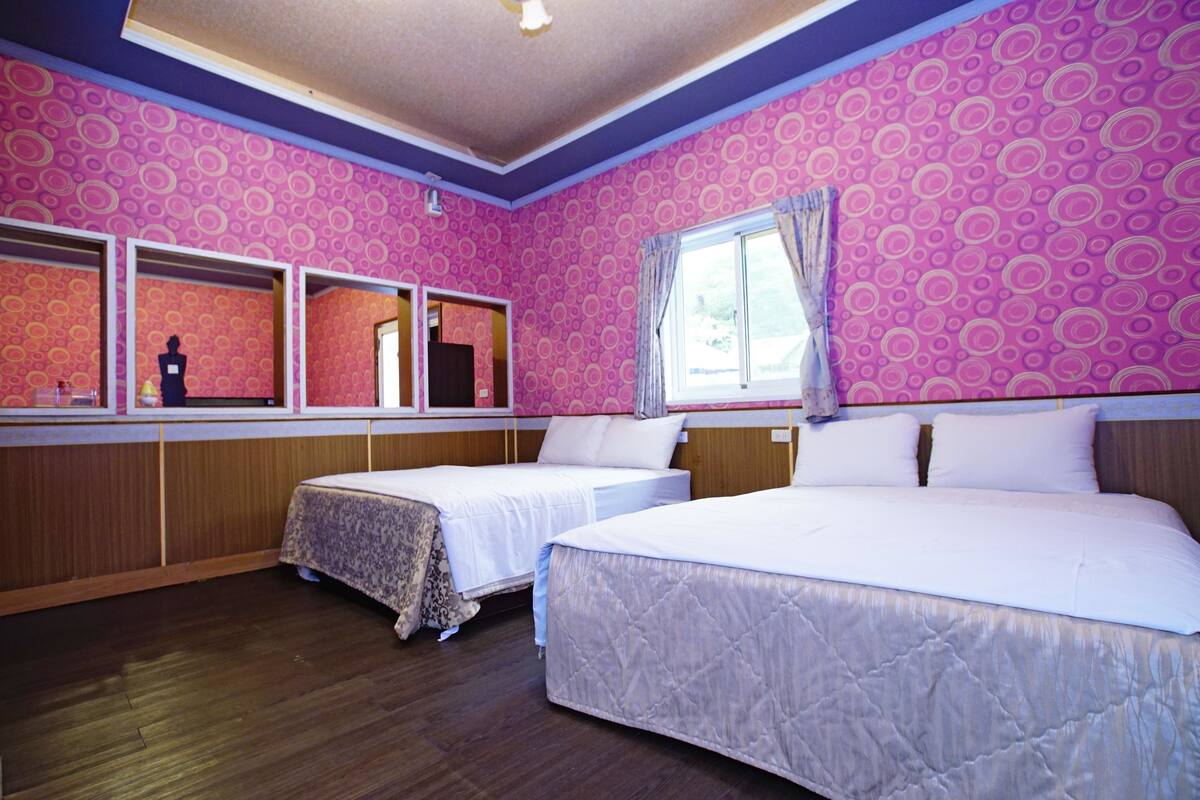 Une chambre avec deux lits, un plancher en bois et une grande fenêtre avec des rideaux.
