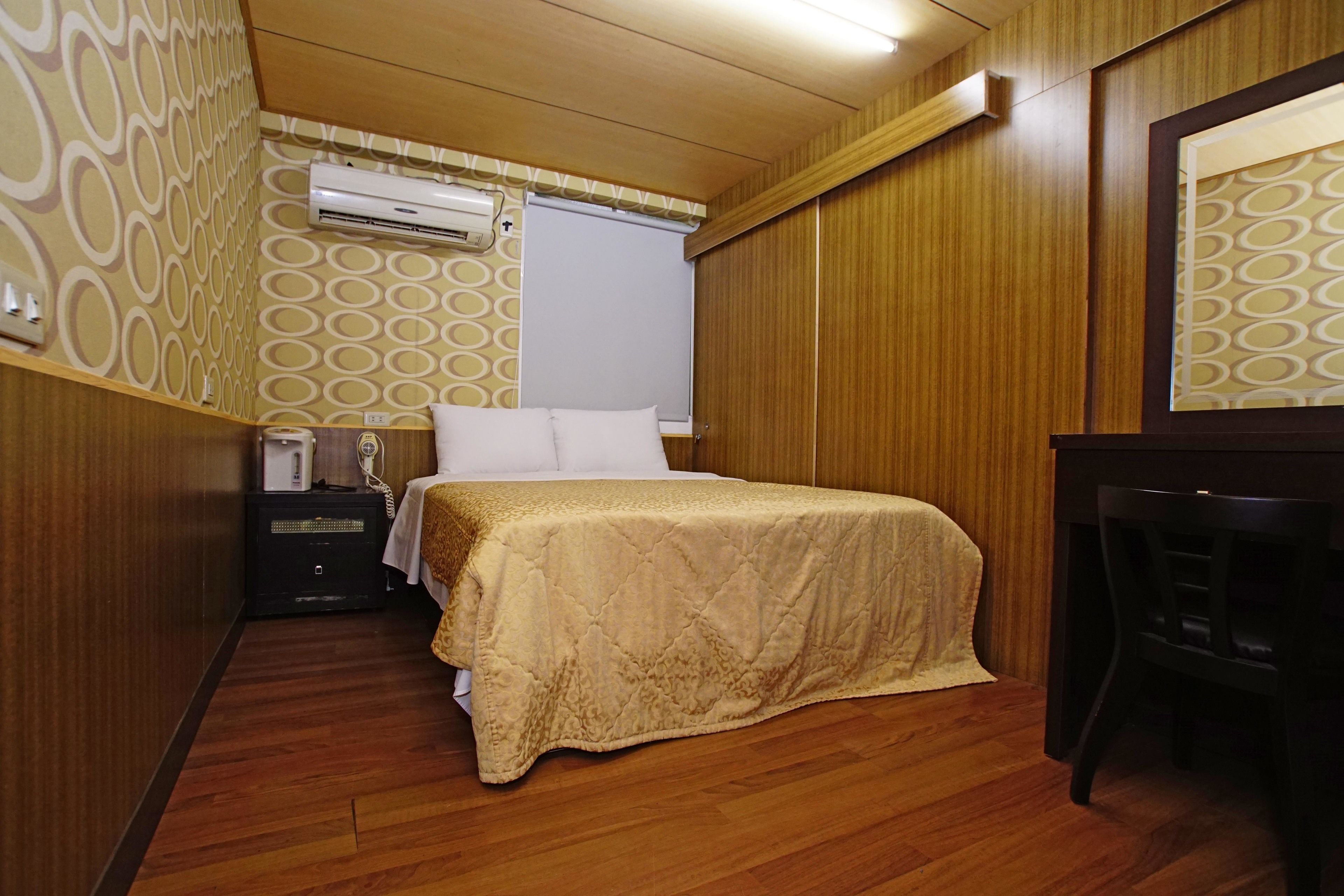 A hotel room with a bed, a desk, an air conditioning unit, and a patterned wall.