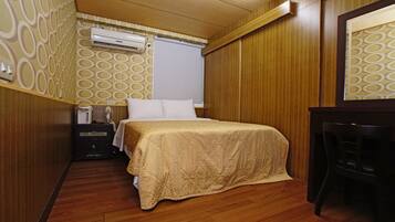 A hotel room with a bed, a desk, an air conditioning unit, and a patterned wall.