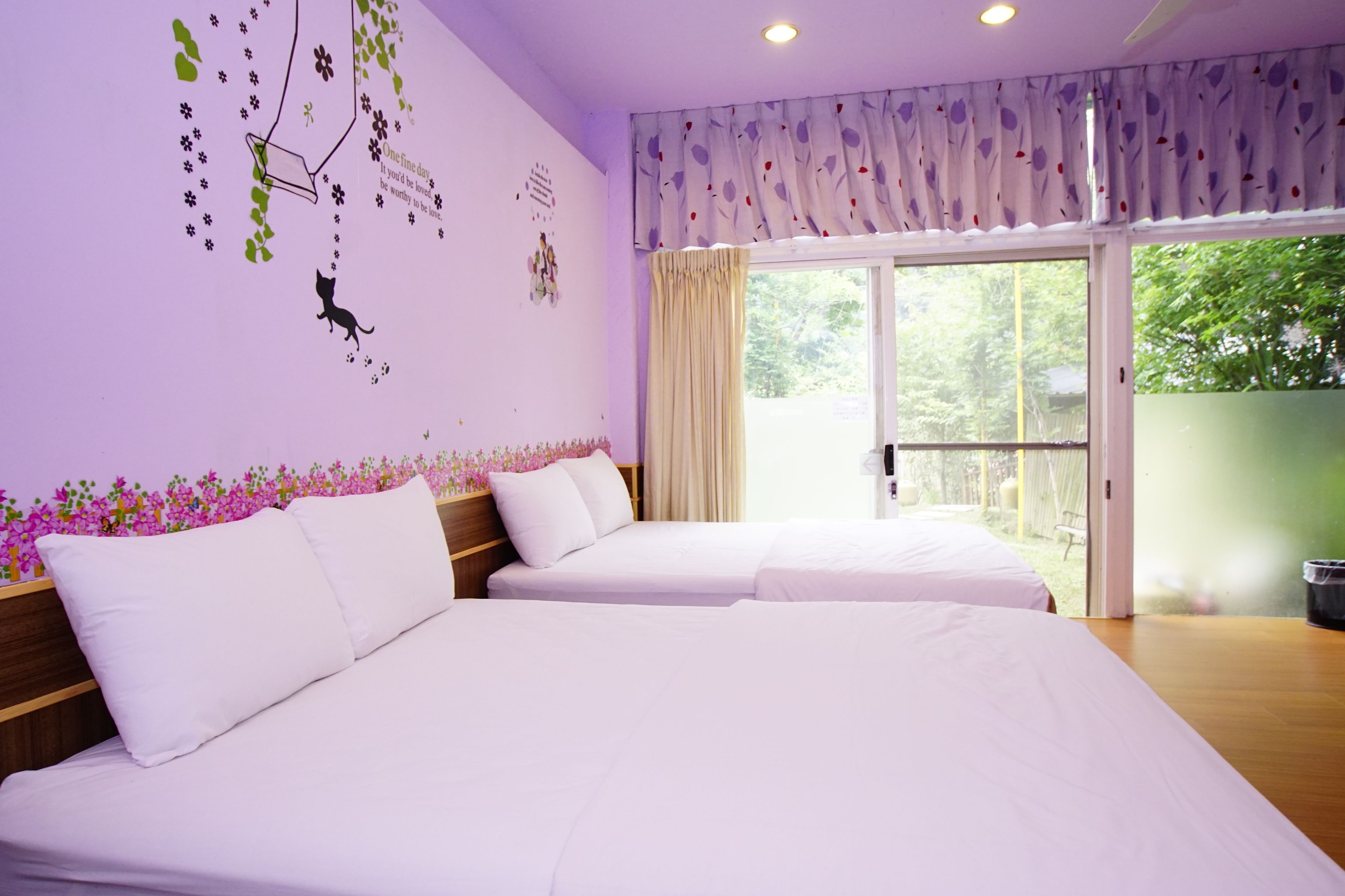 Habitación de hotel con dos camas, un ventanal grande con cortinas, un balcón y una pared decorada con motivos florales.