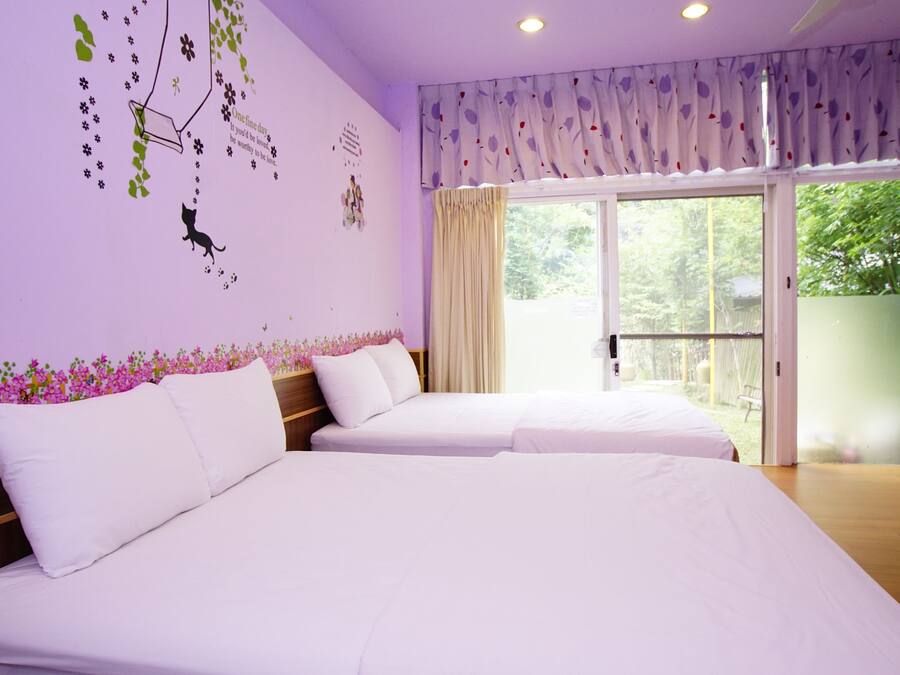 A hotel room with two beds, a large window with curtains, a balcony, and a wall with floral decals.