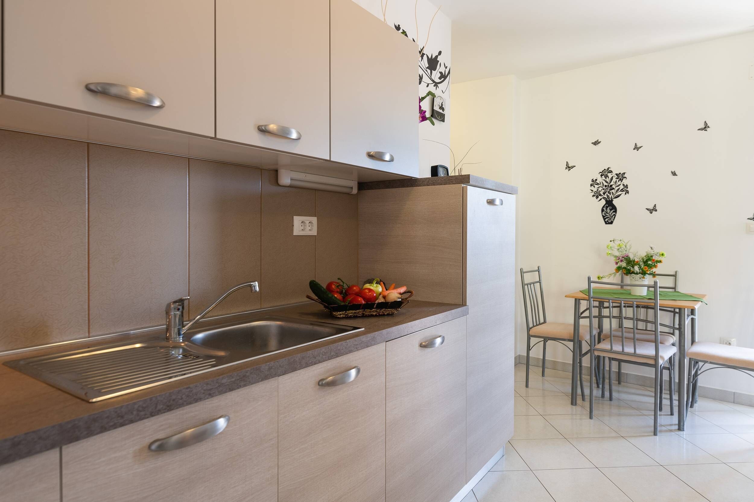 A modern kitchen with a sink, a fruit bowl, and a dining area with chairs and a table.