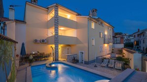 Ein Wohngebäude mit Schwimmbad, Sitzgelegenheiten im Freien und einem gut beleuchteten Balkon.