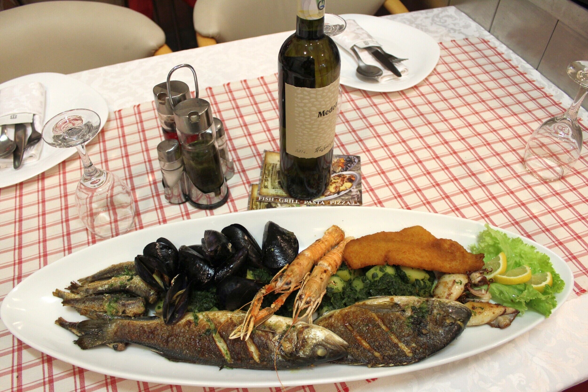 A dining table with a checkered tablecloth, a bottle of wine, and a plate of seafood.