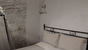 Ein Bett mit weißer Bettdecke und Kissen, ein Metall-Kopfstück und eine weiße Wand mit steinartiger Struktur.