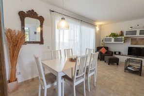 A dining area with a white table and chairs, a mirror, and a hanging light fixture. - House with garden next to the beach with wifi (Es Mercadal)