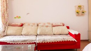 A living room with a red sofa, a glass coffee table, and a wall-mounted air conditioner. - Yi Xin Apartment - Hostel (Xi'an)