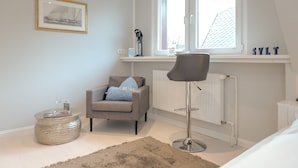 Een moderne slaapkamer met een groot raam, een radiator, een stoel, een ronde salontafel en een lijst met een afbeelding aan de muur.