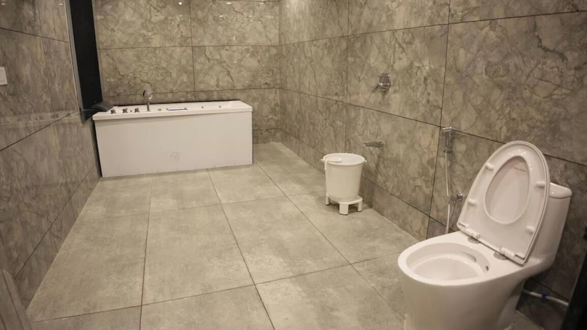 A bathroom with a bathtub, toilet, and a trash bin.