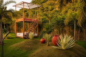 Un pabellón con escalera, cama y un florero rojo en un jardín exuberante.