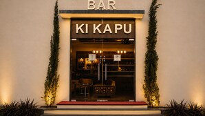 Un bar llamado 'KI KAPU' con un cartel sobre la entrada, un cartel de exhibición y una alfombra roja que conduce a la puerta.