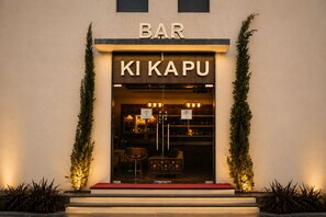 Un bar llamado 'KI KAPU' con un cartel sobre la entrada, un cartel de exhibición y una alfombra roja que conduce a la puerta.