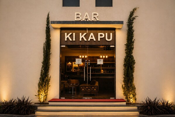 A bar named 'KI KAPU' with a sign above the entrance, a pull-up sign, and a red carpet leading to the door.