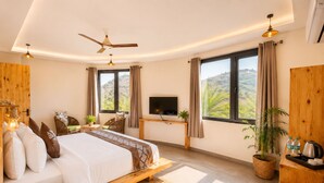 Un dormitorio con cama, televisión, escritorio, ventana con cortinas y una planta.