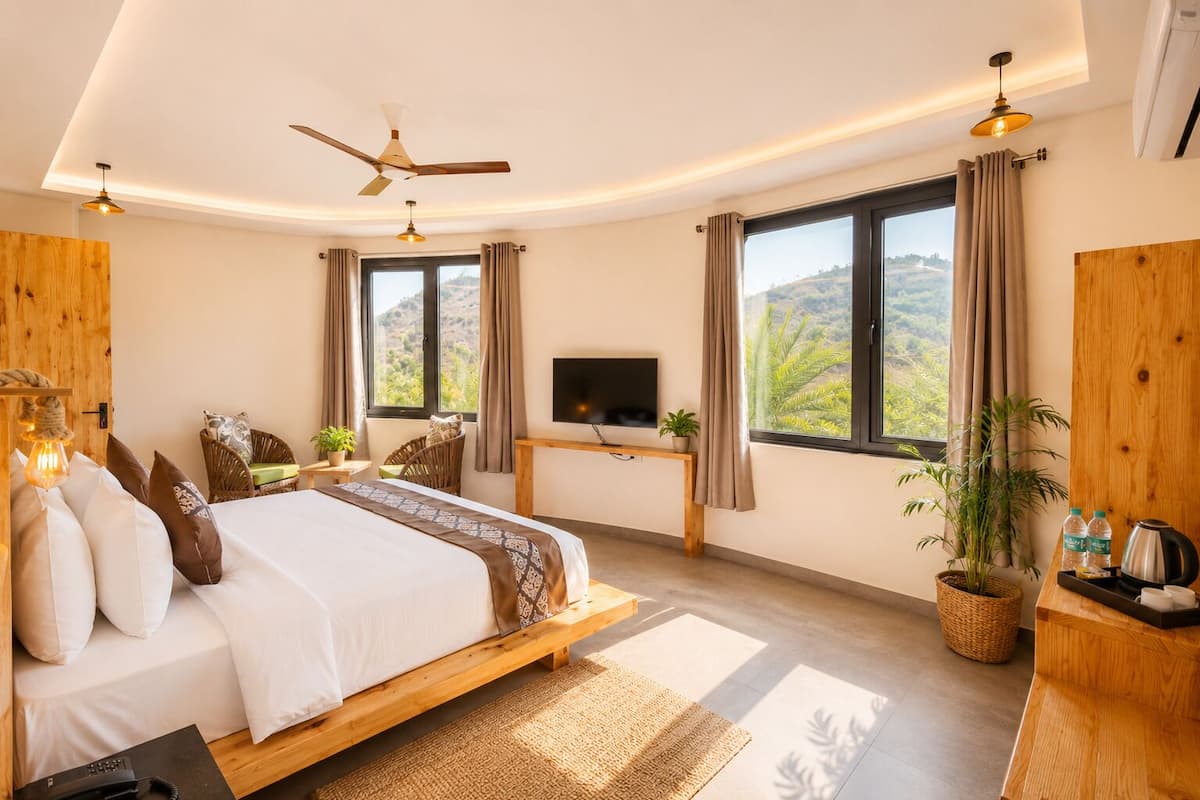 Un dormitorio con cama, televisión, escritorio, ventana con cortinas y una planta.