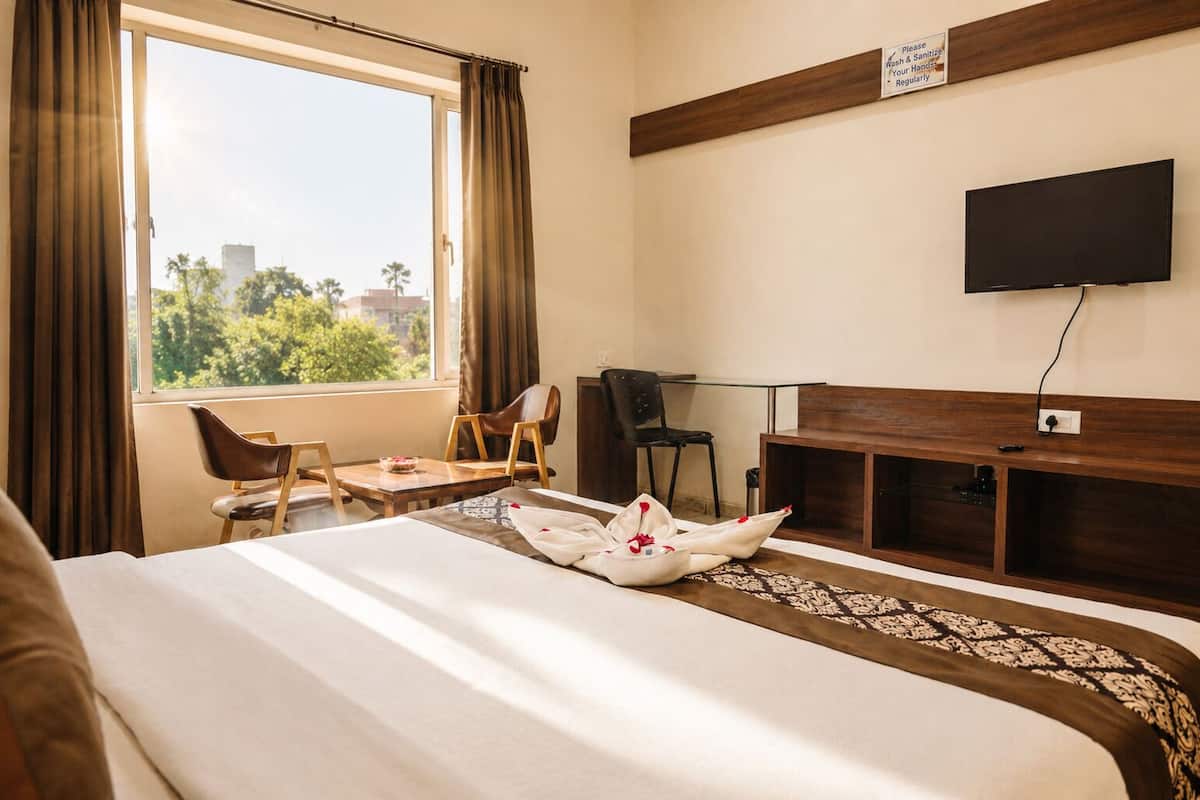 Habitación de hotel con cama, dos sillas, escritorio, televisor y ventana con cortinas.