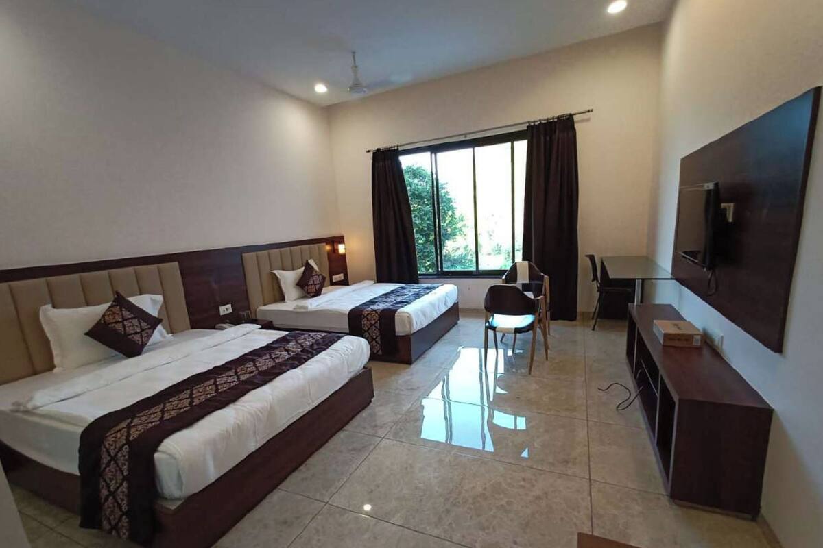 Una habitación de hotel con dos camas, un escritorio, una silla, un televisor y un ventanal con cortinas.