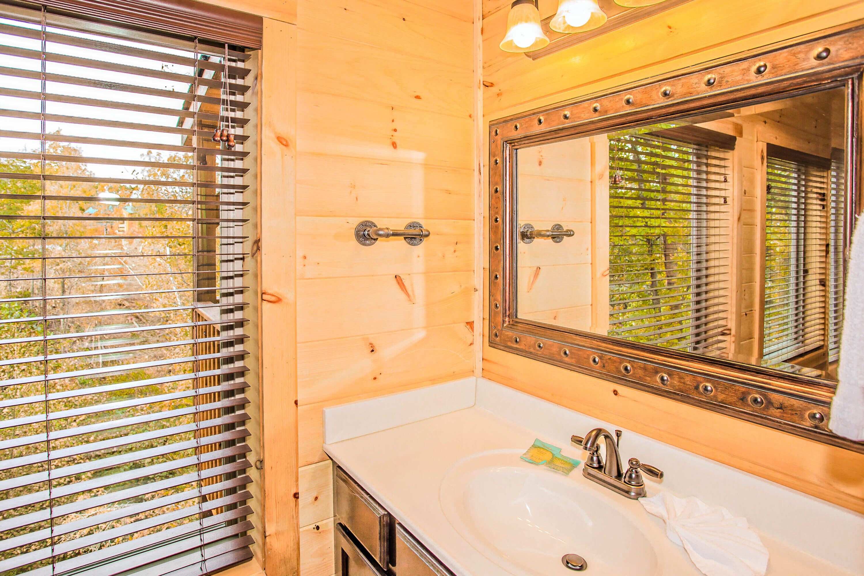 Une salle de bain avec des murs en bois, un grand miroir, un lavabo et une fenêtre avec des stores.