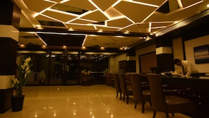 A modern interior with a geometric ceiling design, a reception desk, and a dining area with chairs.