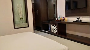 A hotel room with a bed, a TV mounted on the wall, a mirror, and a small table with toiletries.