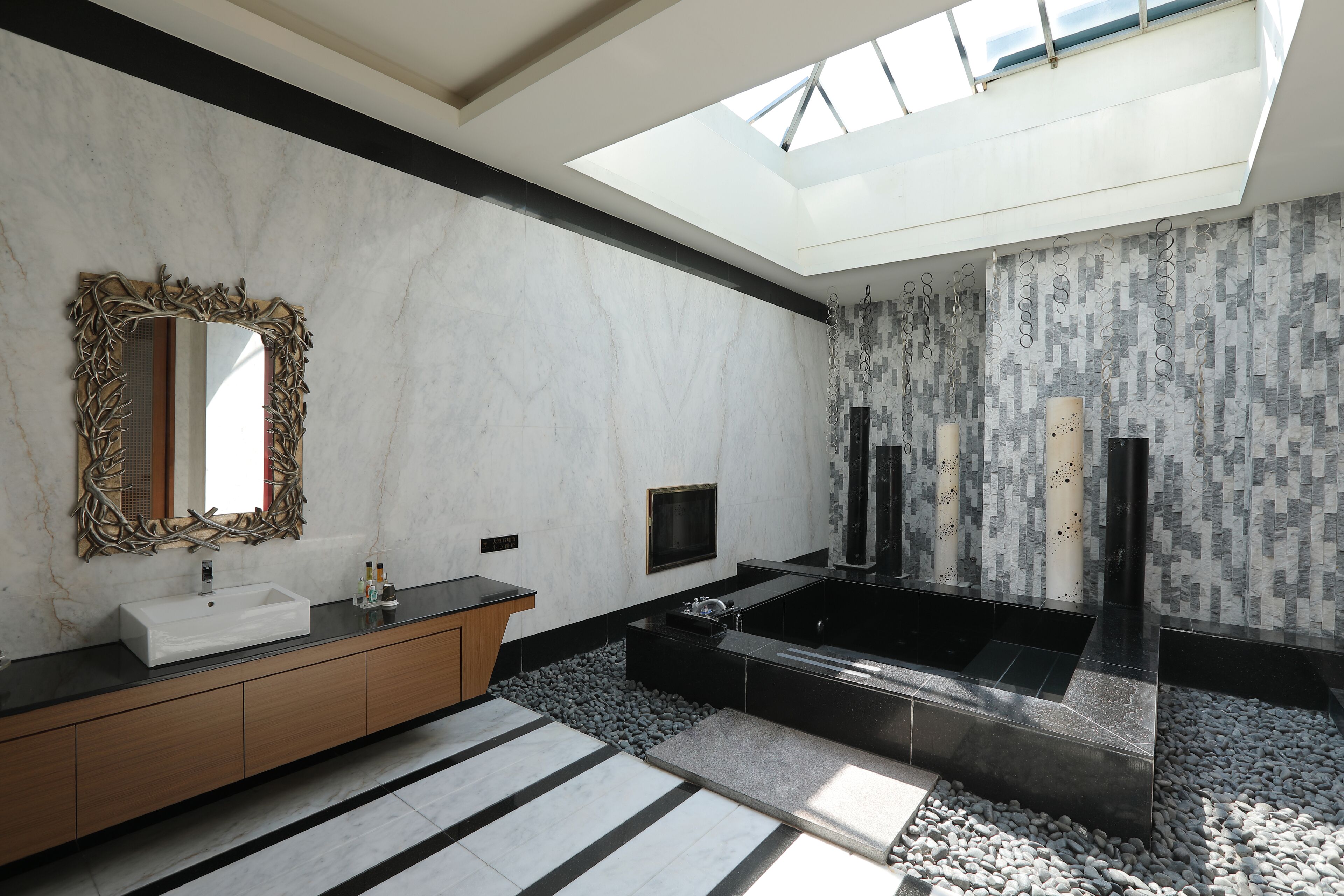 A modern bathroom with a skylight, a large mirror, a white sink, a black bathtub, and a tiled shower area.