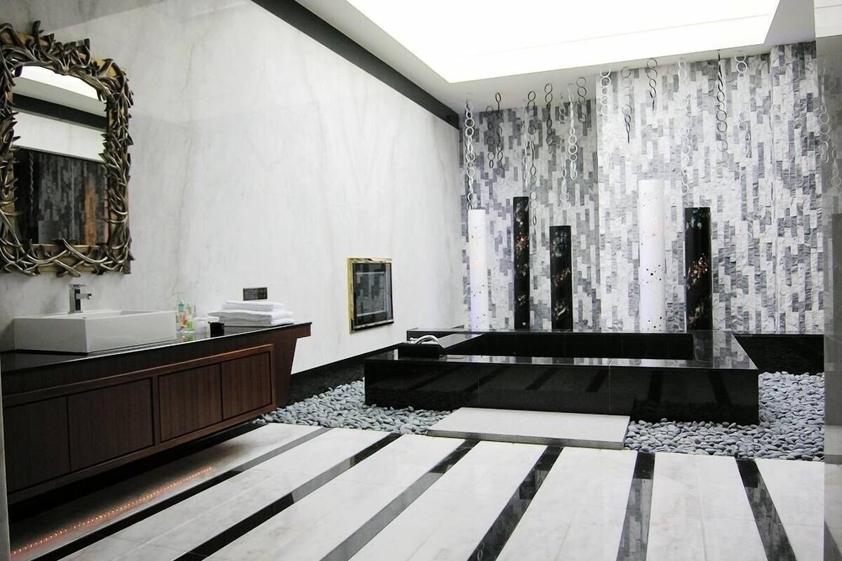 A modern bathroom with a large mirror, a wooden vanity, a black bathtub, and a unique textured wall.