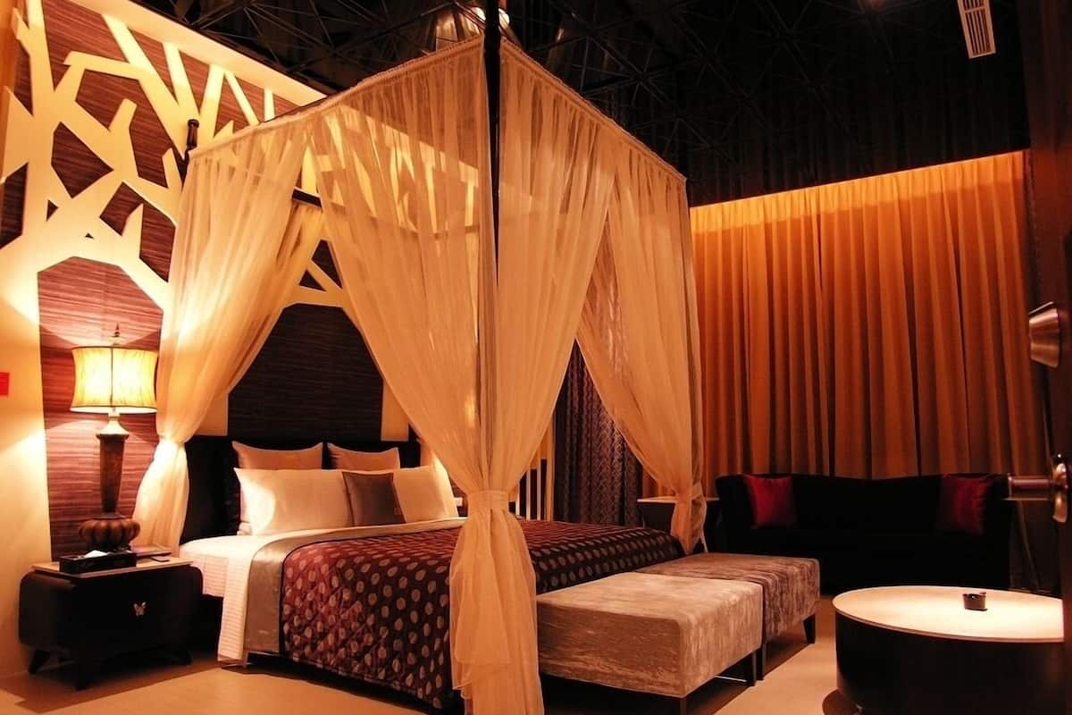 A bedroom with a canopy bed, a bedside table, a chair, and a round table.