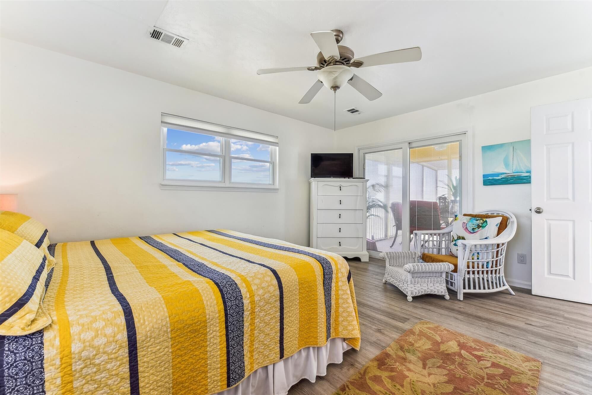 Ein Schlafzimmer mit Bett, Deckenventilator, Kommode, Stuhl und Tür.