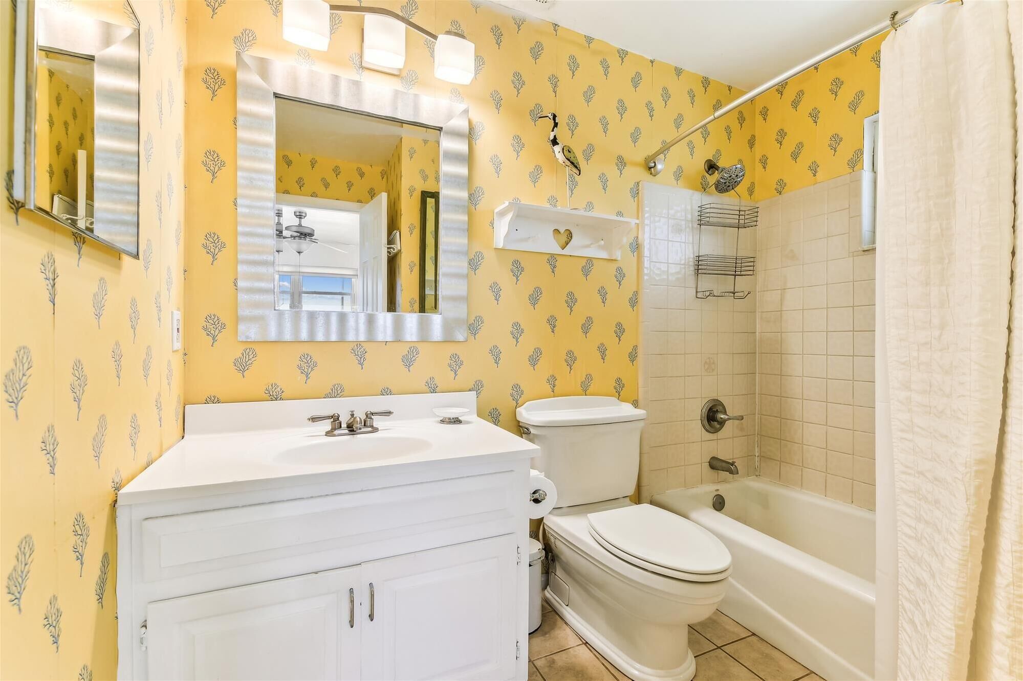 Een badkamer met geel behang met een patroon, een witte wastafel, een toilet en een bad.