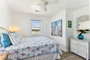 Une chambre à coucher avec un lit, une fenêtre, un tableau, une commode et un ventilateur de plafond.
